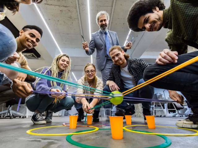 Equipo trasladando una pelota con cuerdas durante una dinámica de team building guiada por un facilitador