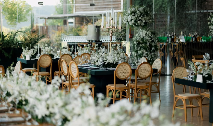 Salón de eventos decorado con flores blancas, candelabro y mesas montadas para un evento corporativo