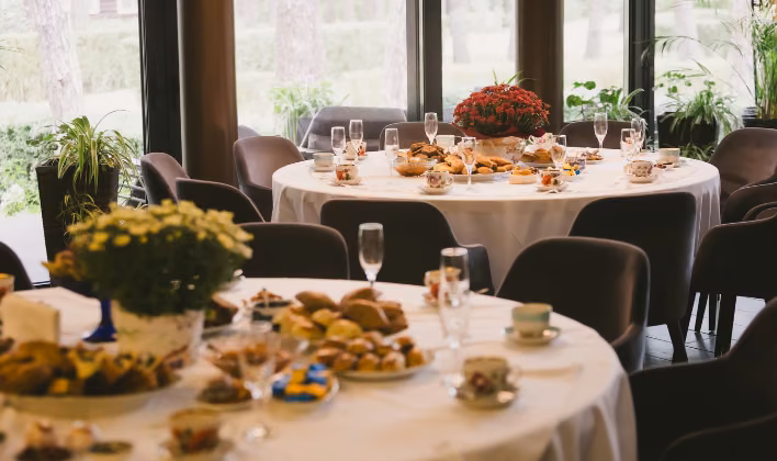 Salón de eventos con mesas redondas montadas junto a ventanales, ideal para celebraciones corporativas