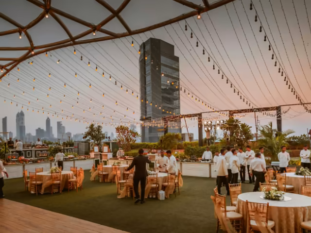 Terraza al aire libre con mesas montadas y luces colgantes lista para un evento corporativo al atardecer