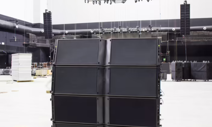 Line array apoyado en el piso de un pabellón vacío de gran volumen, con más arreglos de sonido colgados al fondo