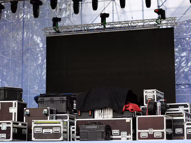 Cases de transporte de equipo técnico apilados frente a la pantalla LED y el truss de un montaje de evento empresarial