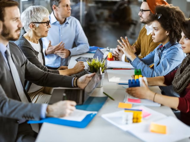 Equipo debatiendo alrededor de una mesa con bloques de construcción y notas adhesivas en un taller empresarial