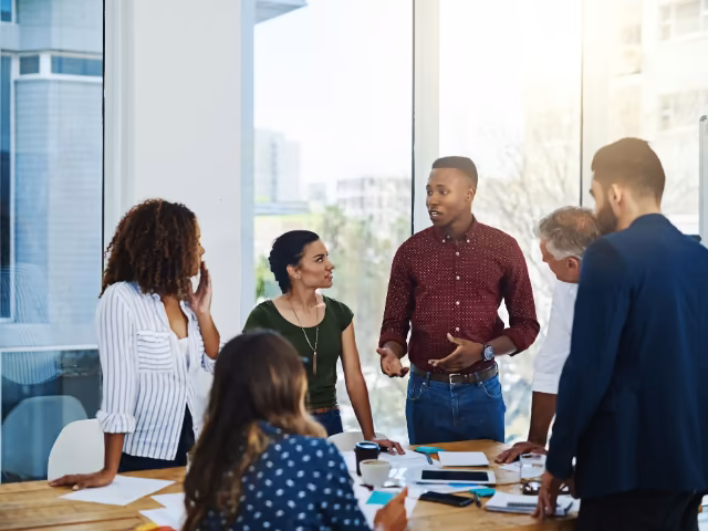 Equipo reunido de pie junto a un ventanal proponiendo ideas para un evento empresarial