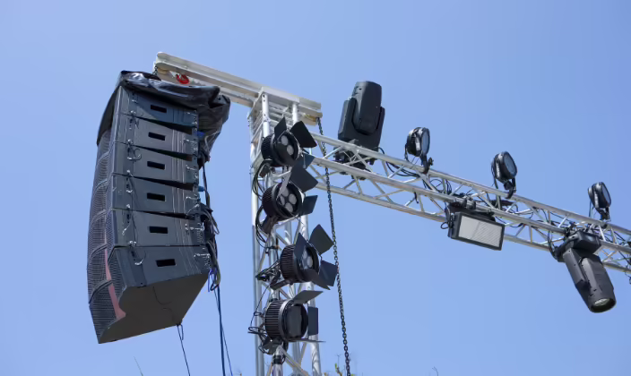 Line array de seis cajas colgado de una estructura truss junto a las luminarias, visto desde abajo contra el cielo
