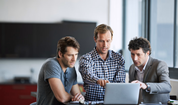 Tres profesionales revisando información en un computador portátil durante la planeación de un evento empresarial