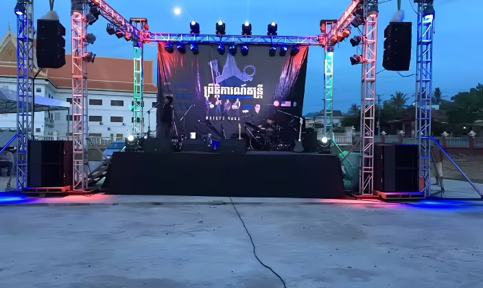 Tarima al aire libre al atardecer con cajas de sonido apiladas sobre torres de truss a cada lado del escenario