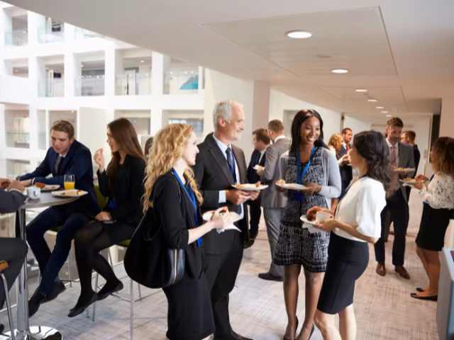 Asistentes con escarapela conversando con plato en mano durante el coffee break de un evento empresarial